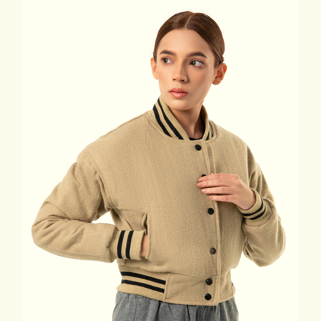 Person wearing a beige crop varsity jacket with black buttons and trim on a white background