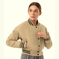 Person wearing a beige crop varsity jacket with black buttons and trim on a white background