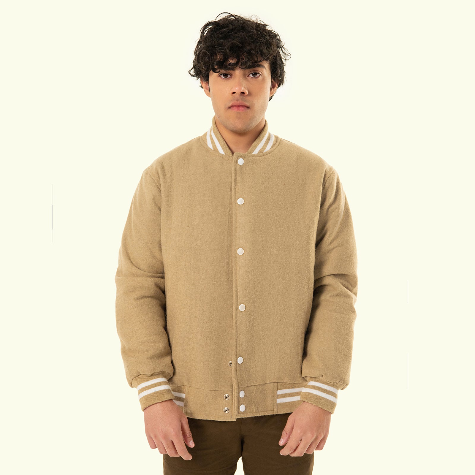Man wearing a beige varsity jacket with white trim on a plain background