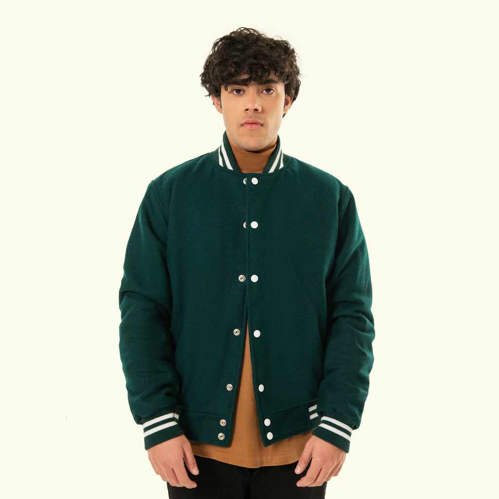 Person wearing a green varsity jacket with white buttons and trim on a white background