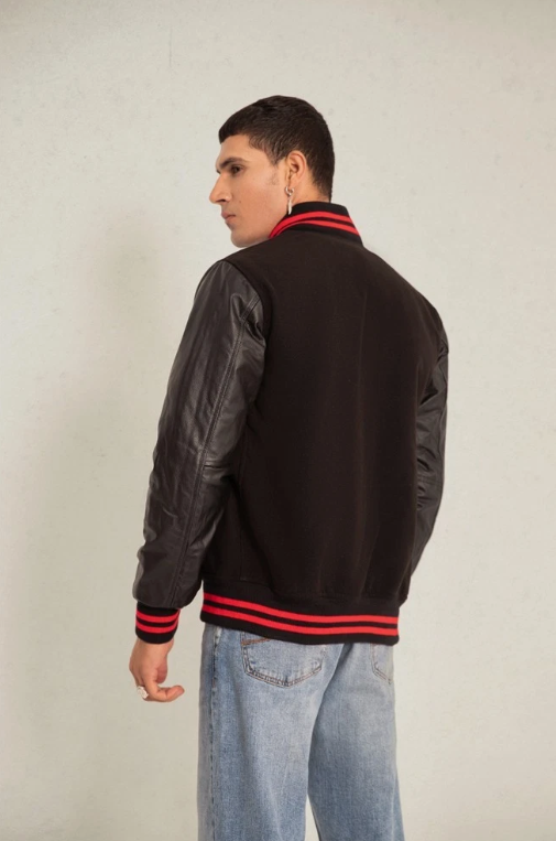 Person wearing a black varsity jacket with red accents on a plain background
