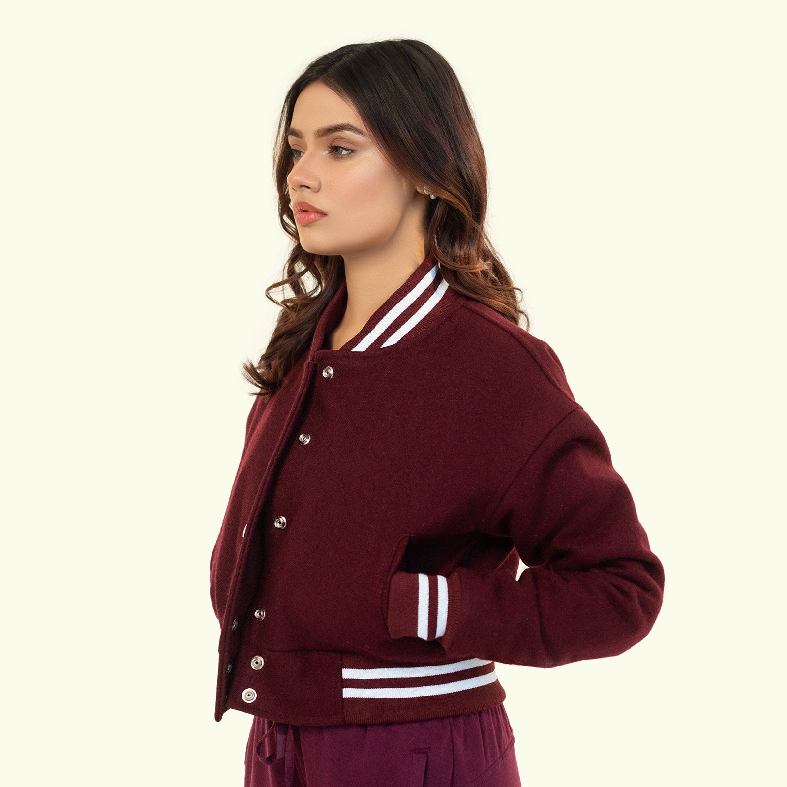 Woman wearing a maroon crop varsity jacket with white accents on a beige background