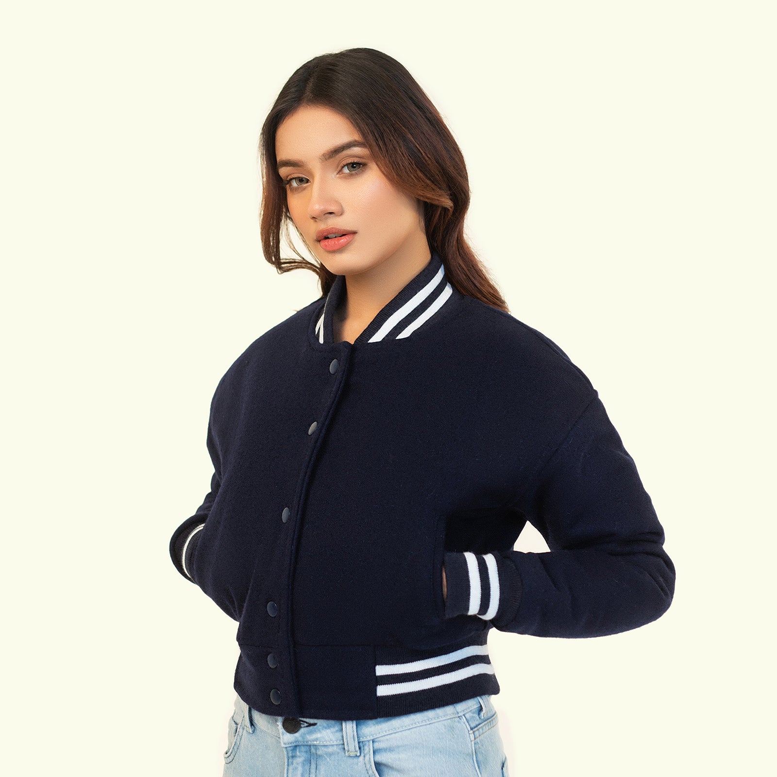 Woman wearing a navy blue varsity jacket with white accents on a beige background