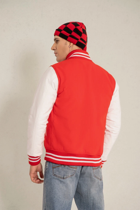 Person wearing a red and white varsity jacket with a checkered beanie on a plain background