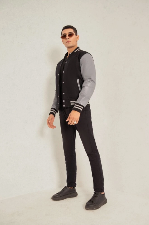 Man wearing a black and gray varsity jacket with black pants on a white background